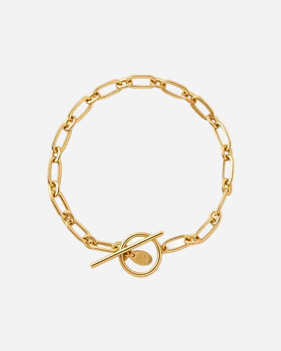 A gold chain bracelet with a toggle clasp, featuring a circular ring and a small engraved heart detail, shown on a plain white background.