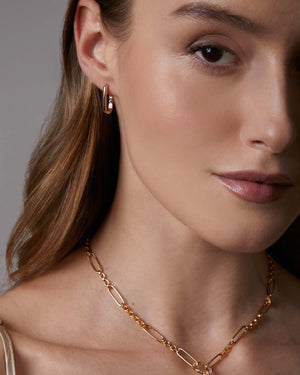 Woman wearing a gold medium size oval hoop earrings on a neutral background