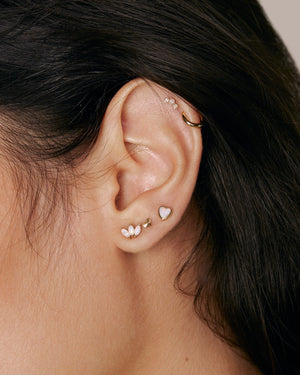 a woman wearing 4 single solid gold stud earrings and a mini huggie hoop earring