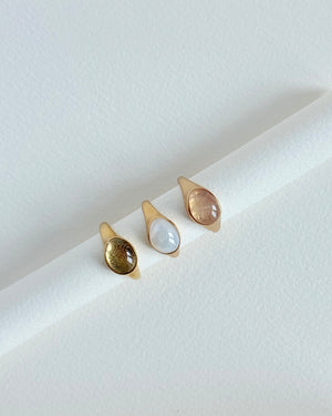 three gold gemstone cabochon ring on a light surface
