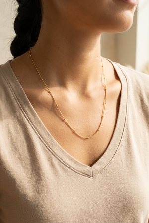 Person wearing a gold satellite chain necklace with a neutral background