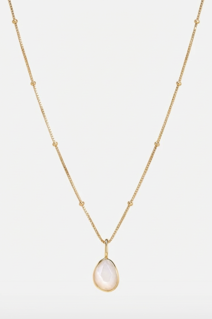 Gold necklace with a teardrop-shaped white moonstone pendant on a light grey background