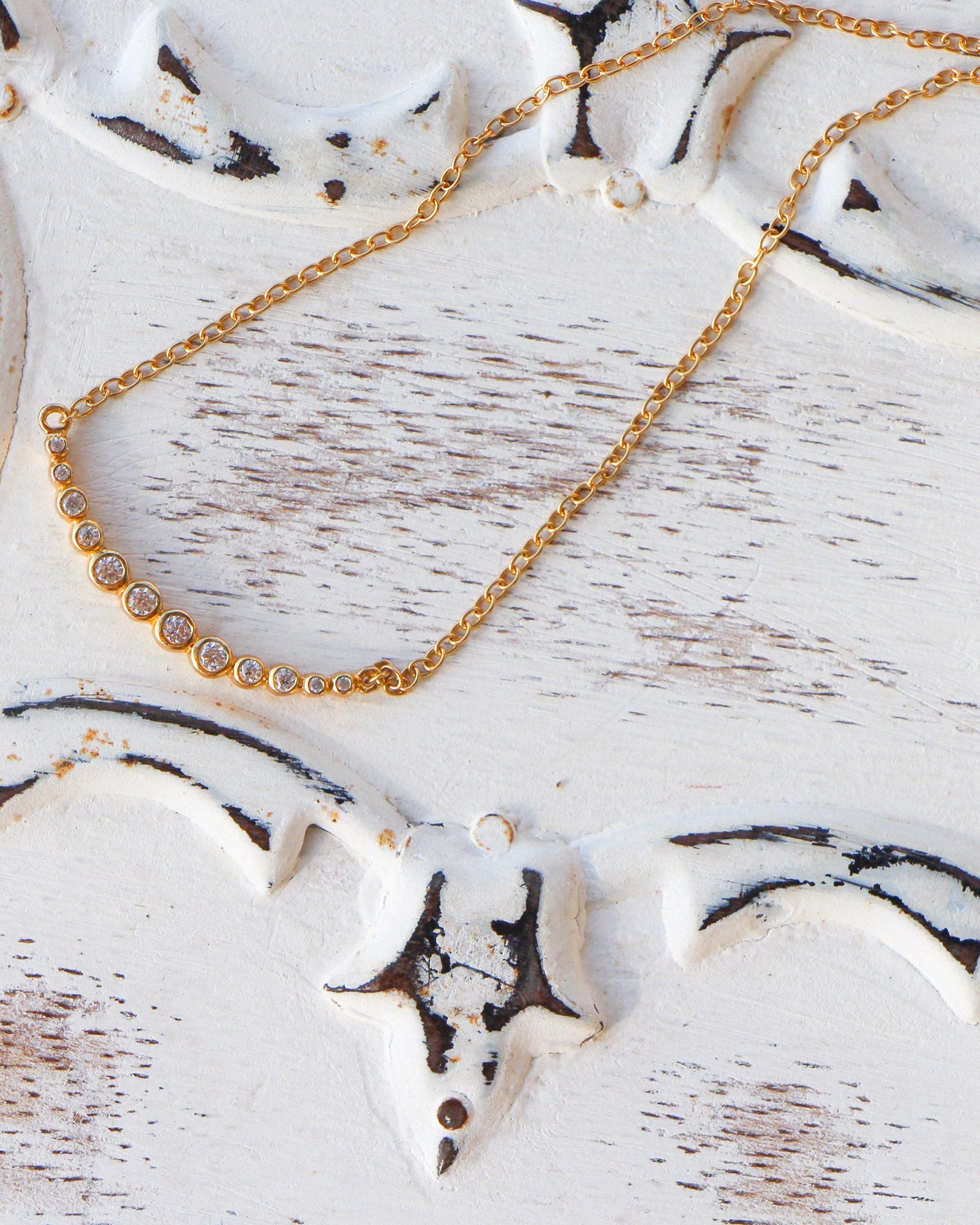 Gold tennis curved bar chain necklace on a light gray background