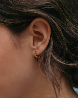 a woman wearing gold flower petal huggie hoop earrings