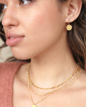 a close up of gold hammered gold vermeil drop earrings on a model's ear