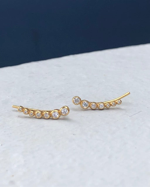 A pair of gold-plated sterling silver ear climbers with cubic zirconia stones set in a curved design.